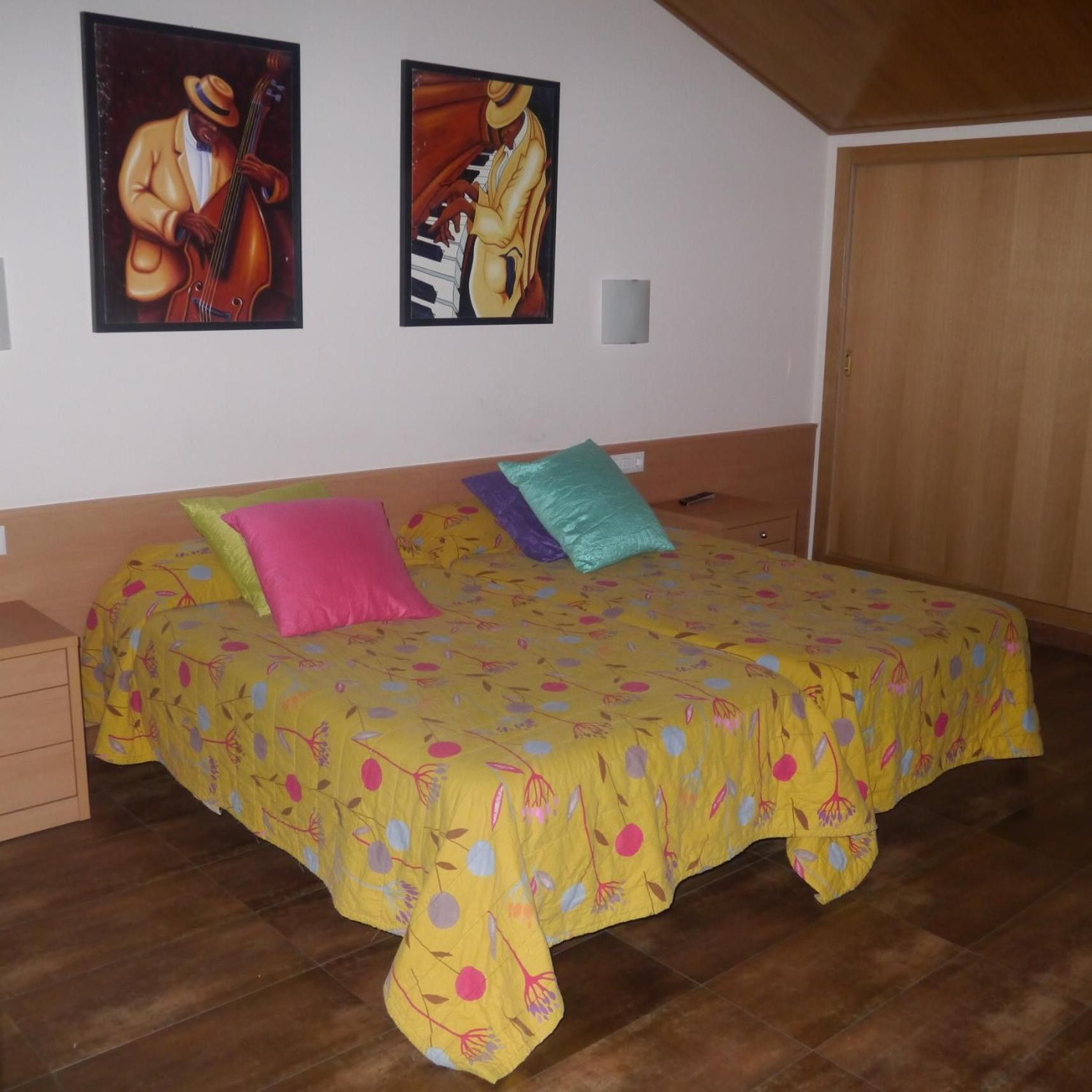 A bedroom with a bed, pillows, a nightstand, and two wall-mounted paintings.
