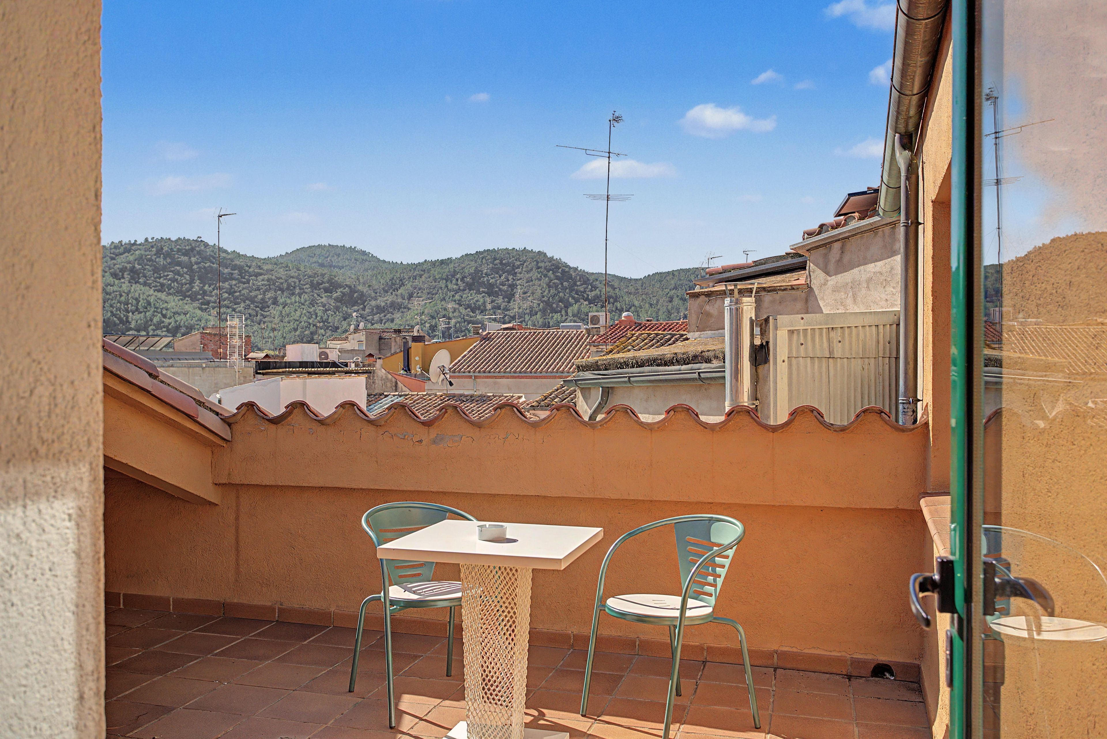 Un balcón con una mesa y dos sillas, con vistas a una colina con edificios.
