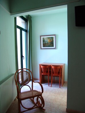 Una habitación con una silla de mimbre, una mesa con sillas, un cuadro en la pared y una ventana con cortinas.
