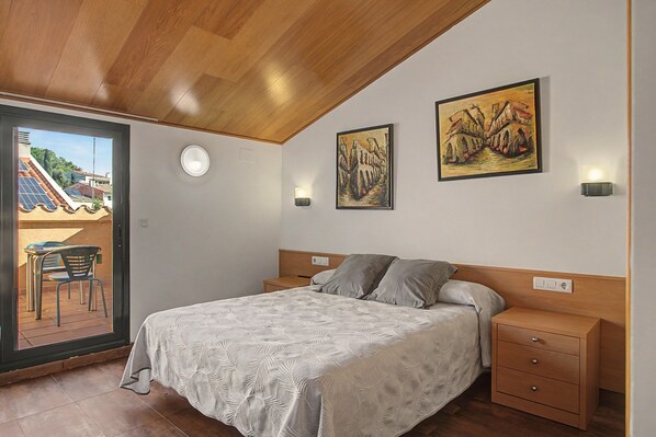 A bedroom with a bed, a nightstand, a wall-mounted light, and two paintings.