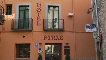 Un hotel llamado 'HOTEL PIRXO' con un cartel sobre la entrada, zona de estar al aire libre con mesas y sillas, y una pared de piedra en un lateral.