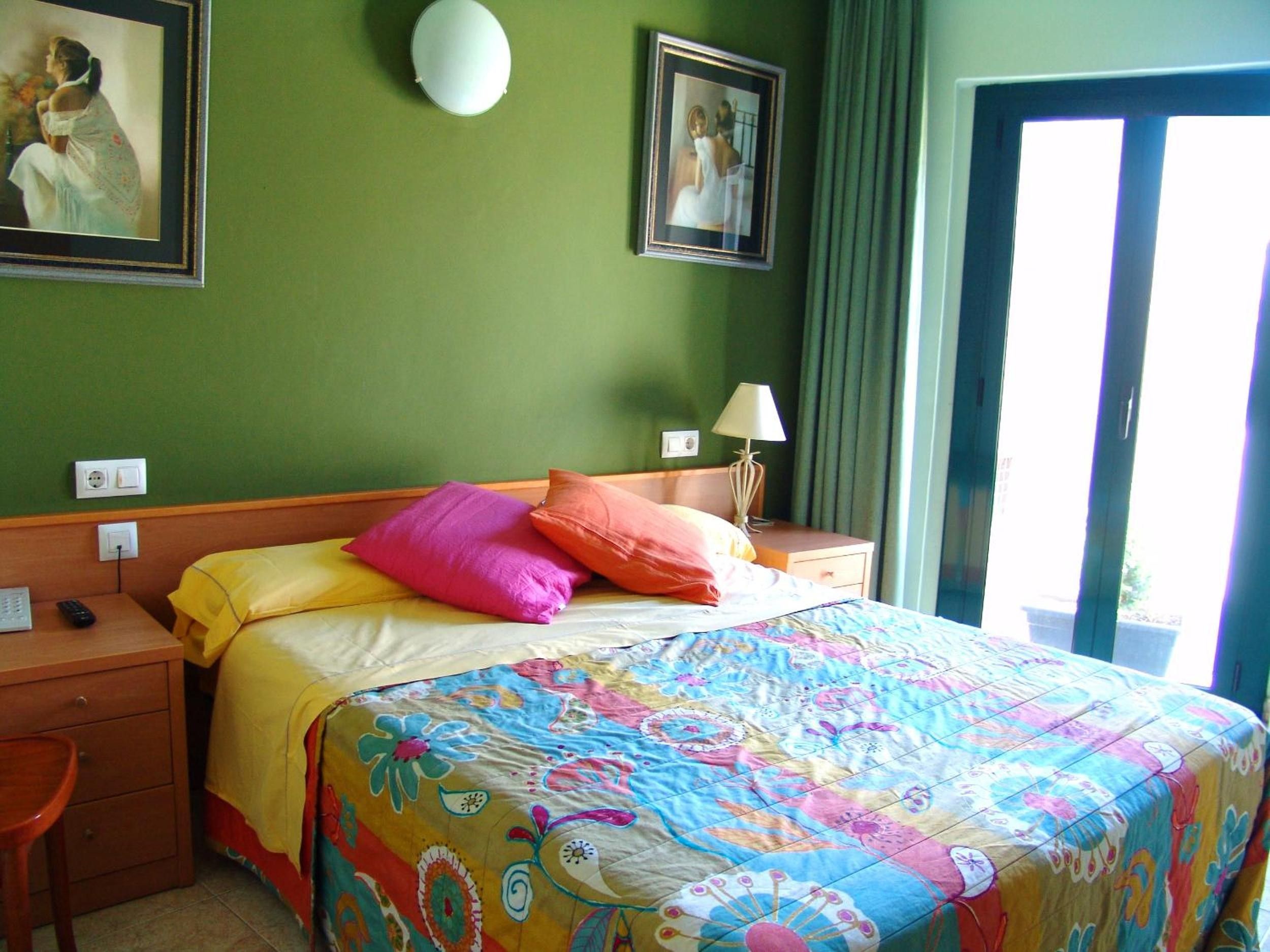 Una habitación de hotel con una cama, una mesita de noche, una lámpara y dos cuadros en la pared.