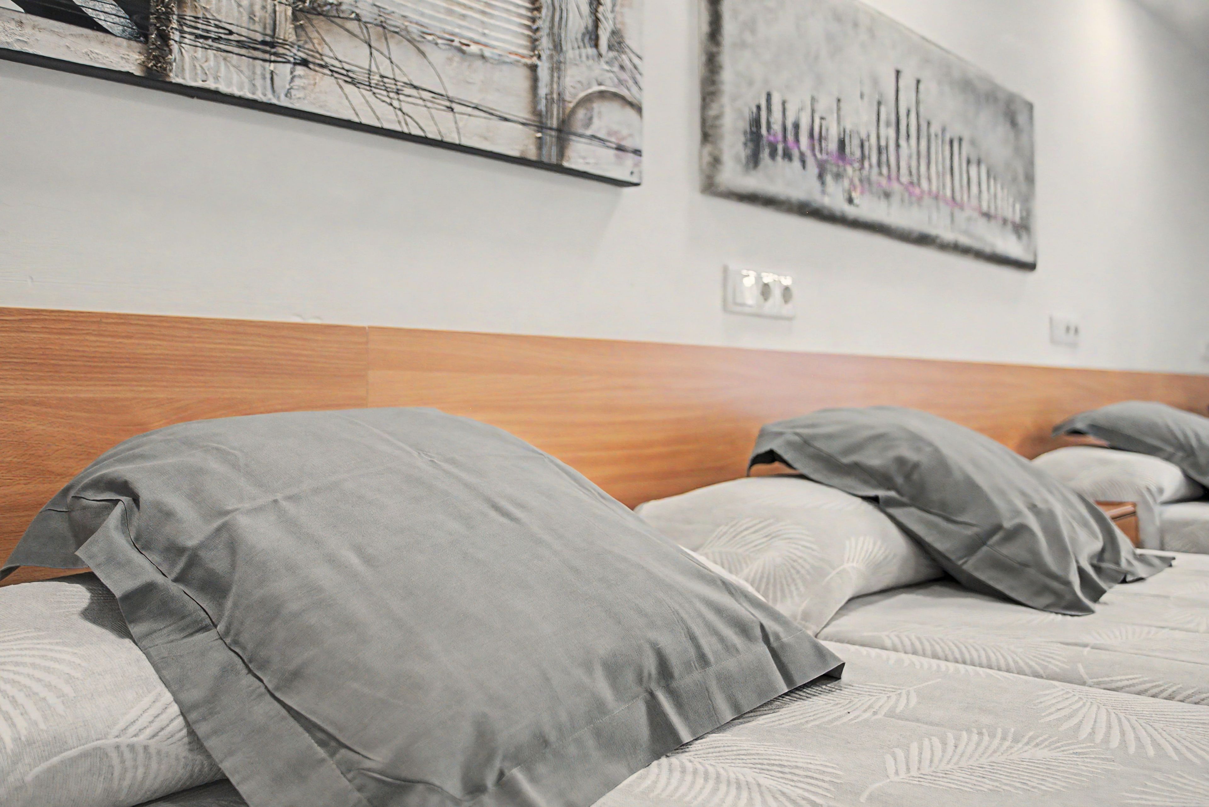 Una habitación de hotel con cabecera de madera, ropa de cama gris y dos obras de arte en la pared.