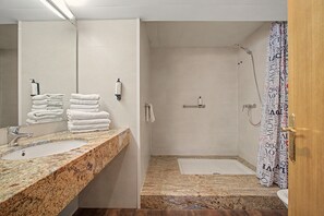 A bathroom with a sink, stacked towels, a shower, and a toilet.