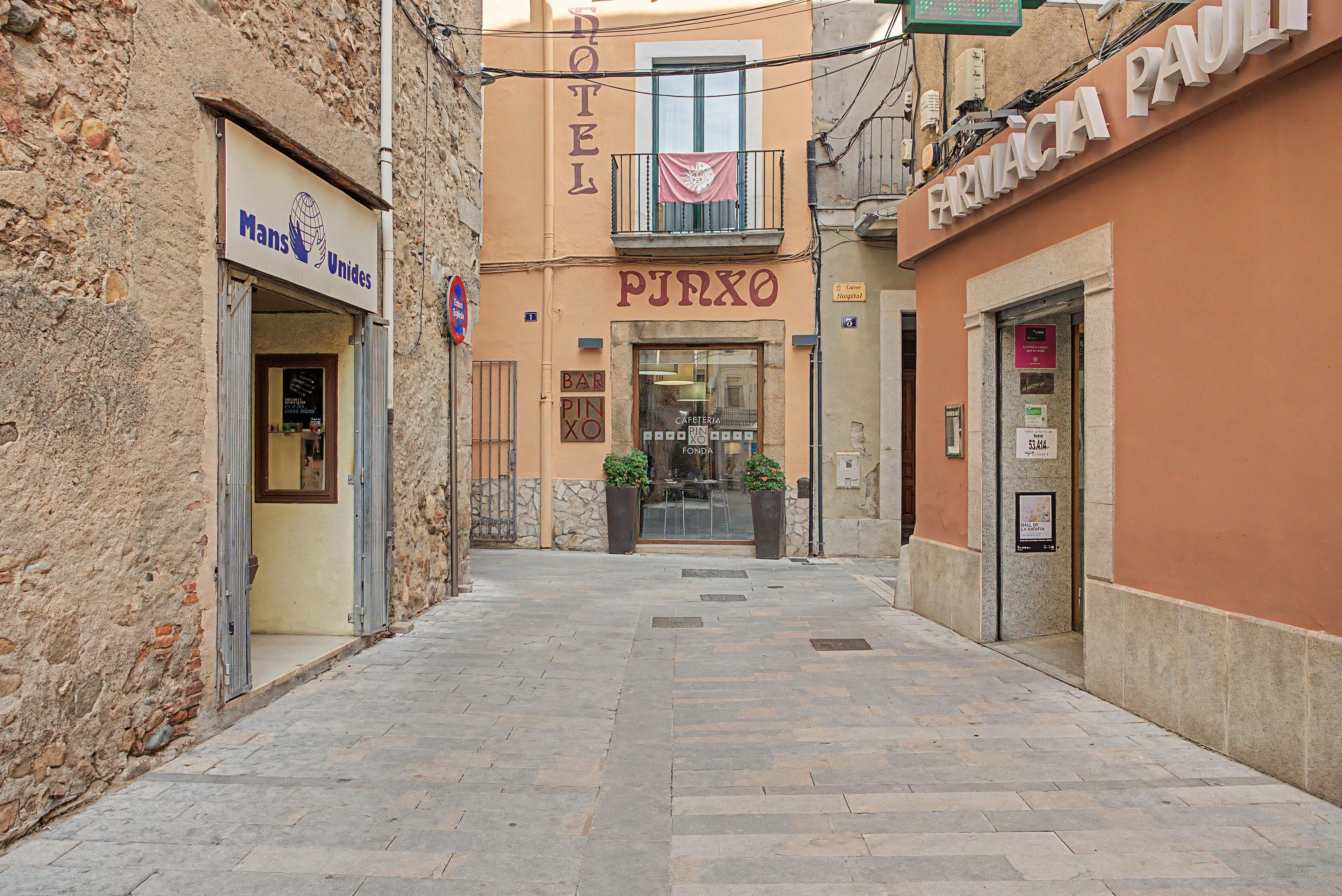 Una calle estrecha flanqueada por un hotel llamado 'HOTEL PIZZO' y una farmacia 'FARMACIA'.