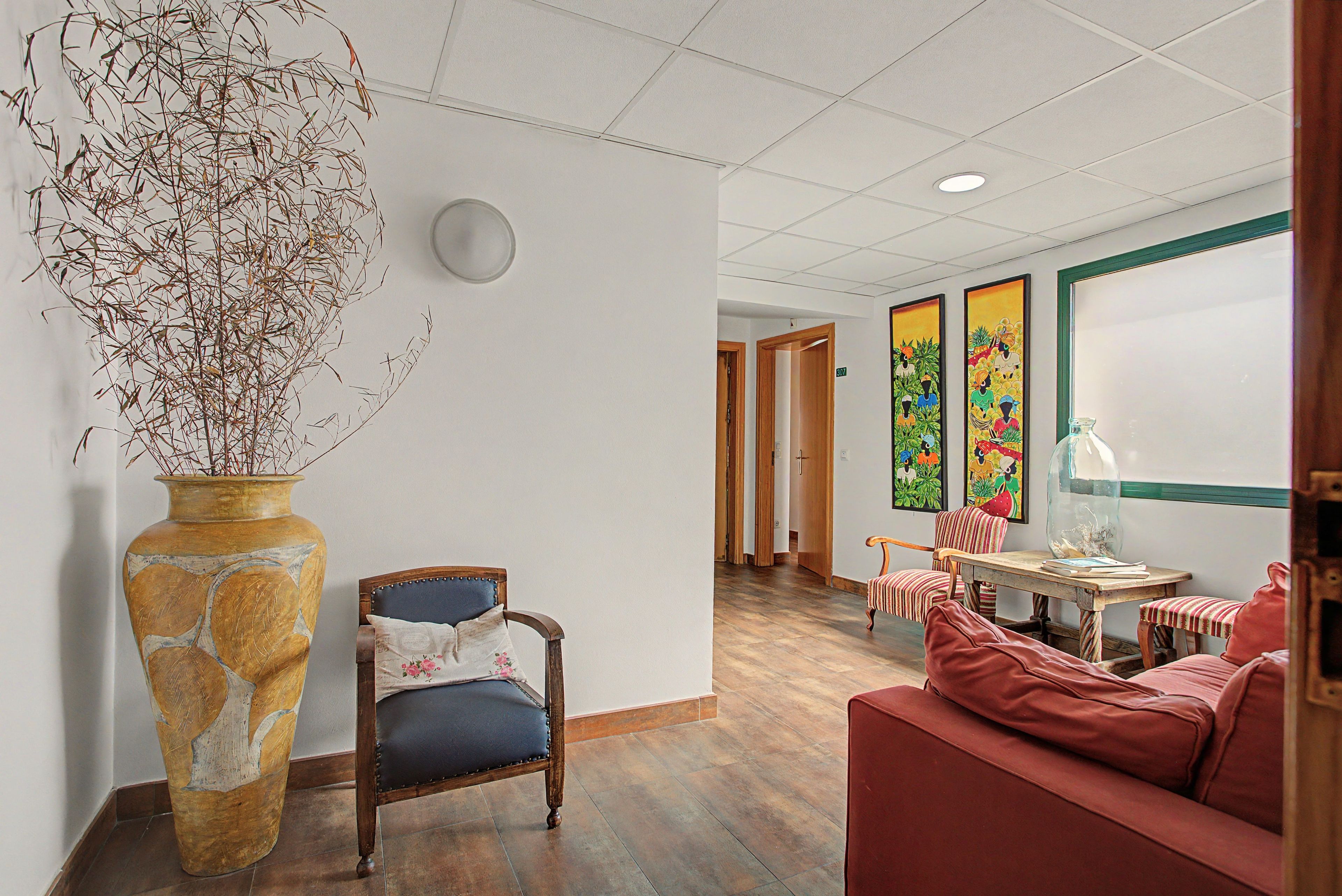 Una habitación con un jarrón grande, una silla, un sofá, una mesa con una cúpula de cristal y obras de arte en la pared.