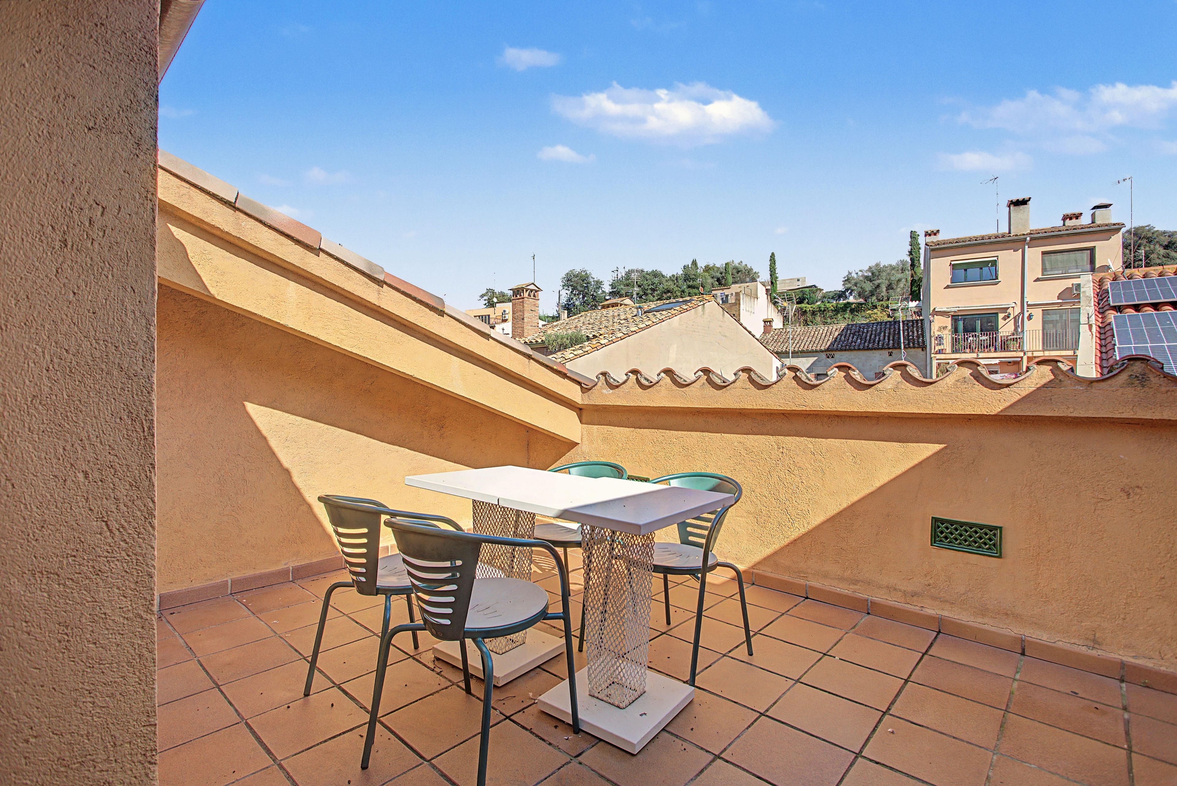 Una terraza con una mesa y sillas, suelo de baldosas y vistas de edificios circundantes.