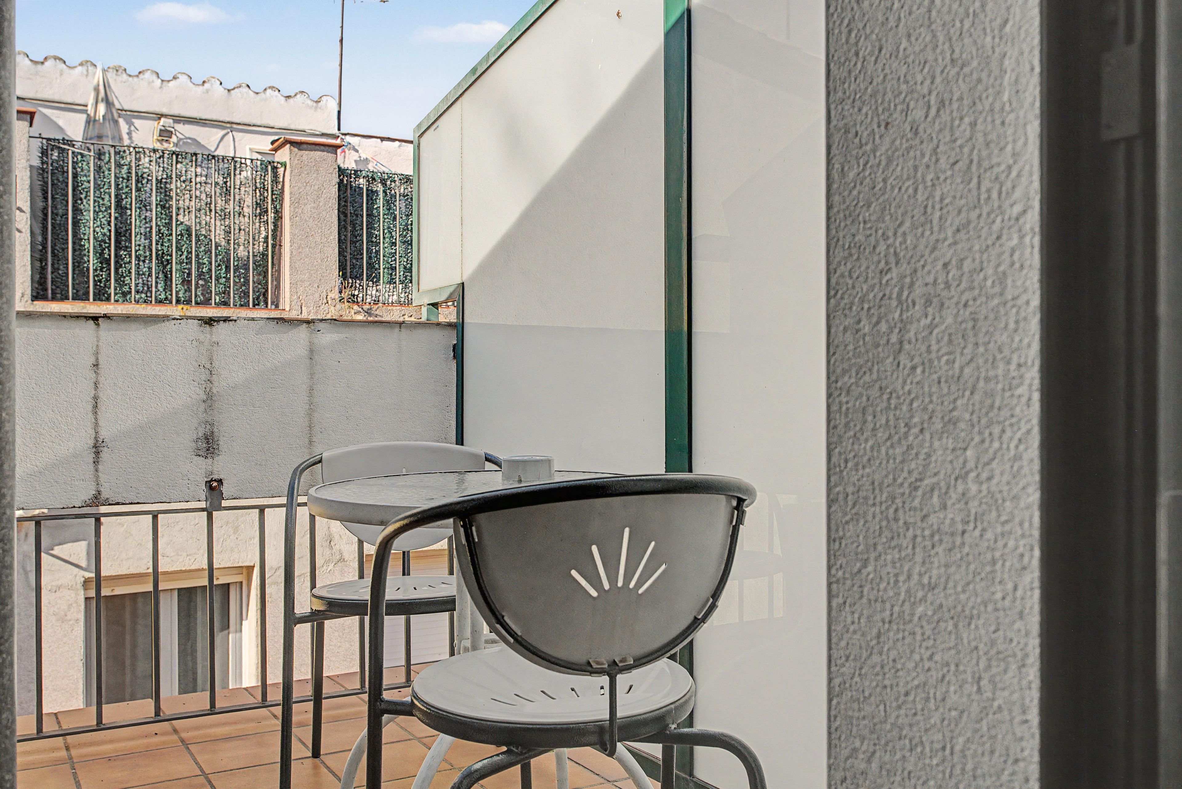 Un balcón con una mesa y sillas, una barandilla de metal y una pared blanca.