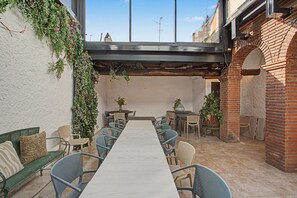 An outdoor patio with a long table and chairs, surrounded by brick walls and greenery.