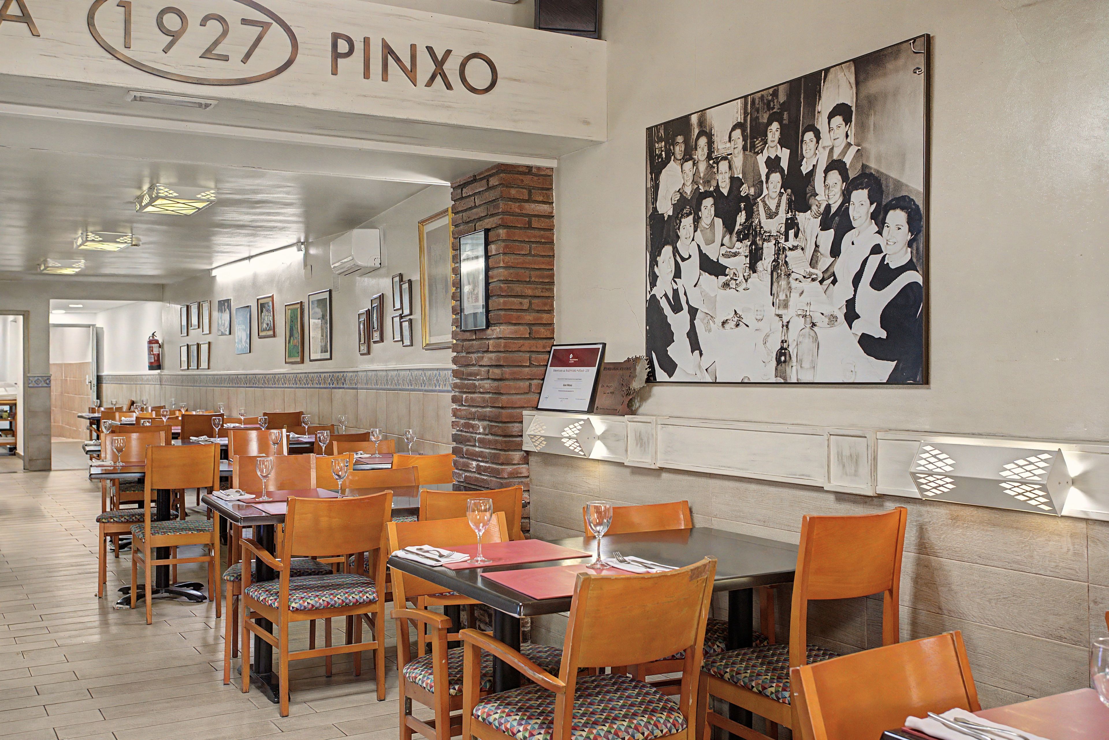Interior de restaurante con mesas y sillas de madera, cuadros en las paredes y una fotografía blanco y negro de época.