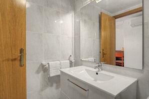 A modern bathroom with a white sink, a mirror, and a wooden door.