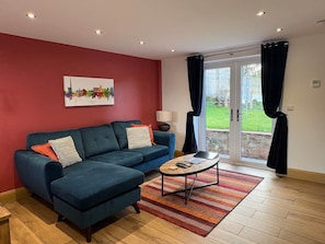 A living room with a blue sofa, a coffee table, and a cityscape painting on the wall. - Myrtle Cottage-Hot tub. Sky TV. Relaxing. Romantic. Couples (Carlisle)