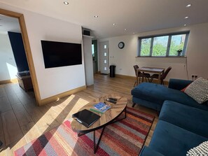 A modern living room with a blue sofa, a coffee table, and a flat-screen TV mounted on the wall. - Myrtle Cottage-Hot tub. Sky TV. Relaxing. Romantic. Couples (Carlisle)
