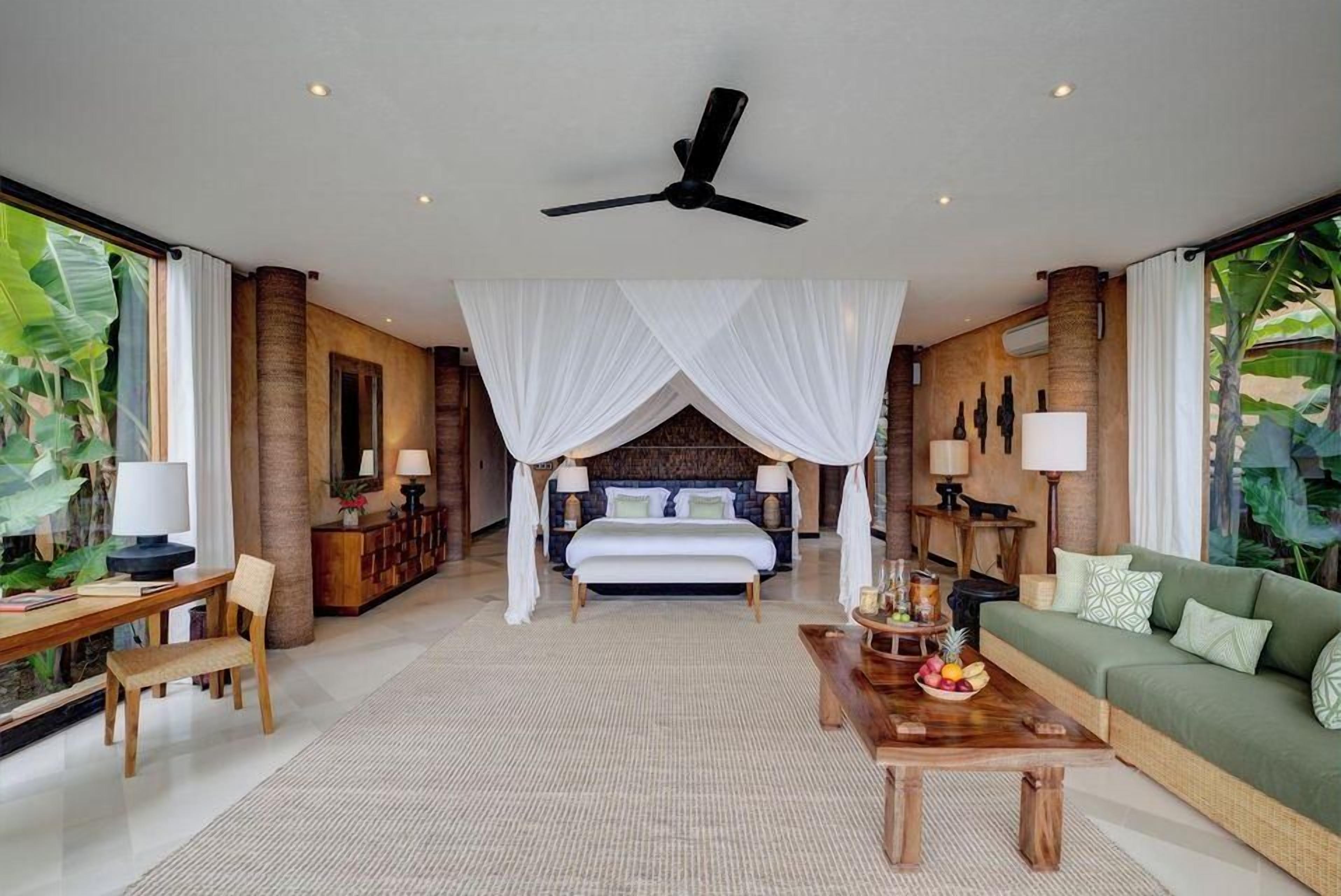 A spacious bedroom with a canopy bed, a sitting area with a coffee table, and a view of tropical foliage.