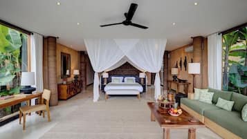A spacious bedroom with a canopy bed, a sitting area with a coffee table, and a view of tropical foliage.