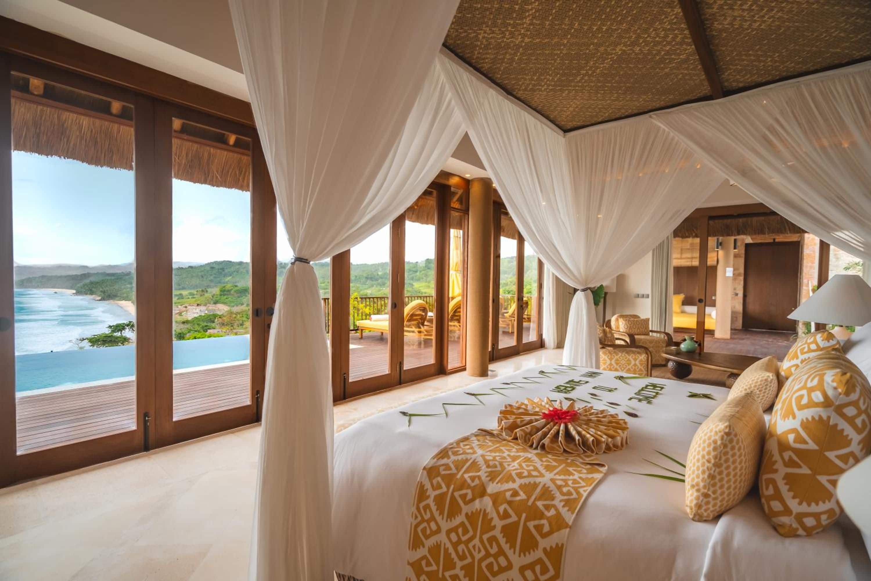 Un dormitorio amplio con una cama grande, vista al océano y un balcón con mobiliario exterior.