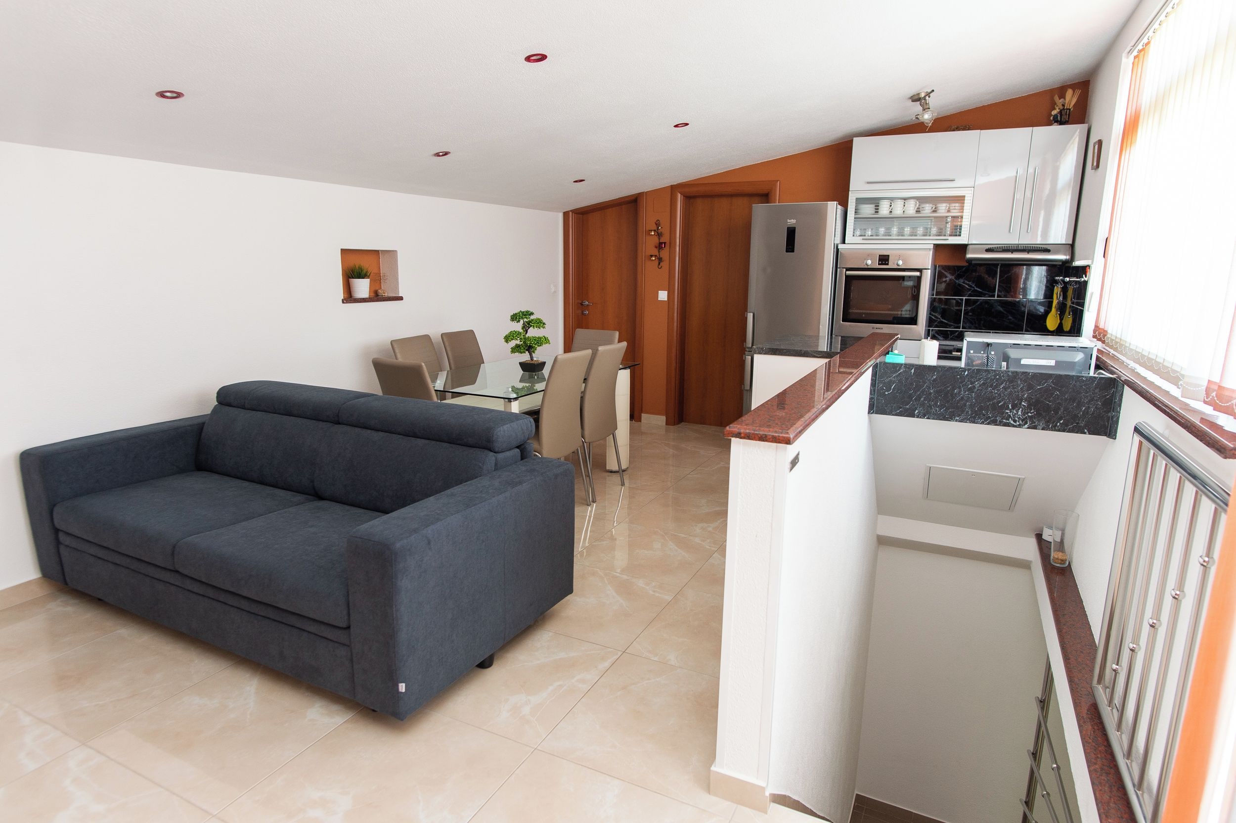 Un espace de vie compact comprenant un canapé, une table à manger avec des chaises, un coin cuisine et une porte donnant sur une autre pièce.