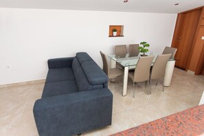 A modern living room with a glass-top dining table, beige chairs, a dark blue sofa, and a small potted plant on the wall. - Penthouse apartment for 4+2 people. Private hot tub on your own terrace. (Podglavica)