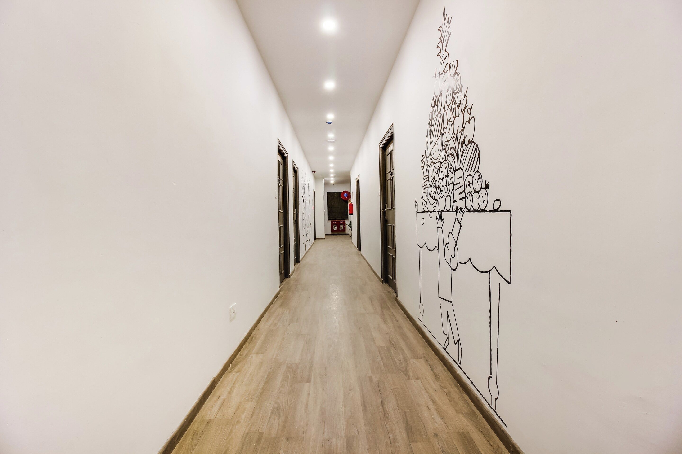 Un pasillo con piso de madera, paredes blancas y un mural en la pared derecha.
