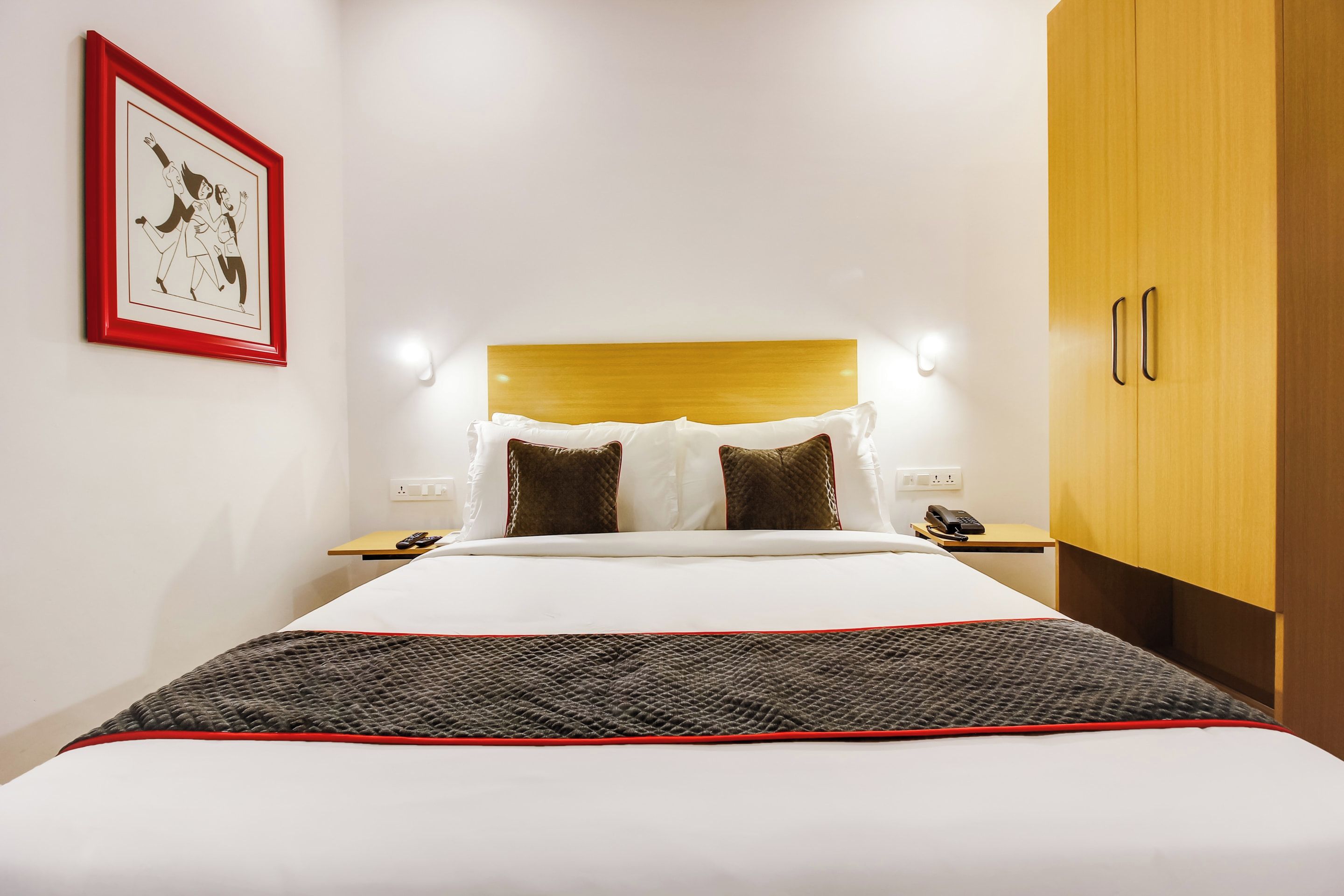 Habitación de hotel con cama, mesitas de noche, armario y un cuadro en la pared.