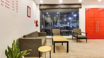 Rebost d'hotel amb un sofà, cadires, una taula petita, una planta en test i un extintor, i una porta vermella.
