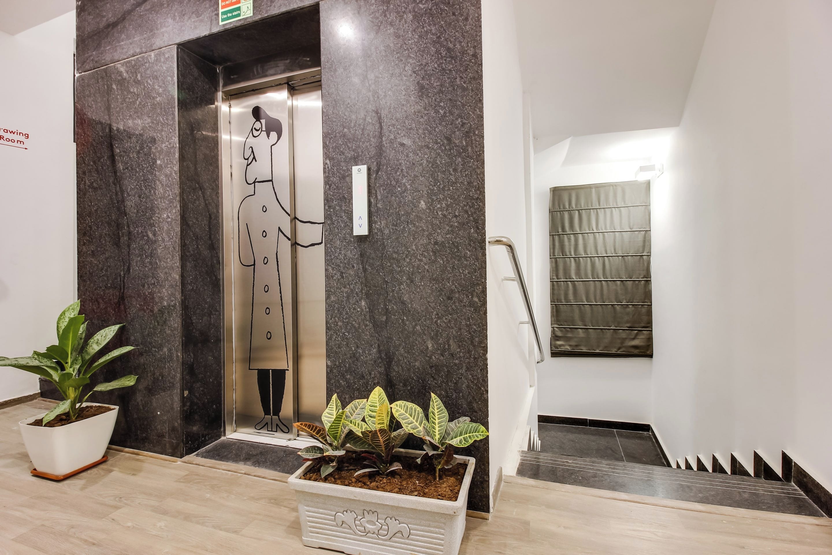 An elevator with a wall-mounted sign, a potted plant, and a staircase with a handrail.