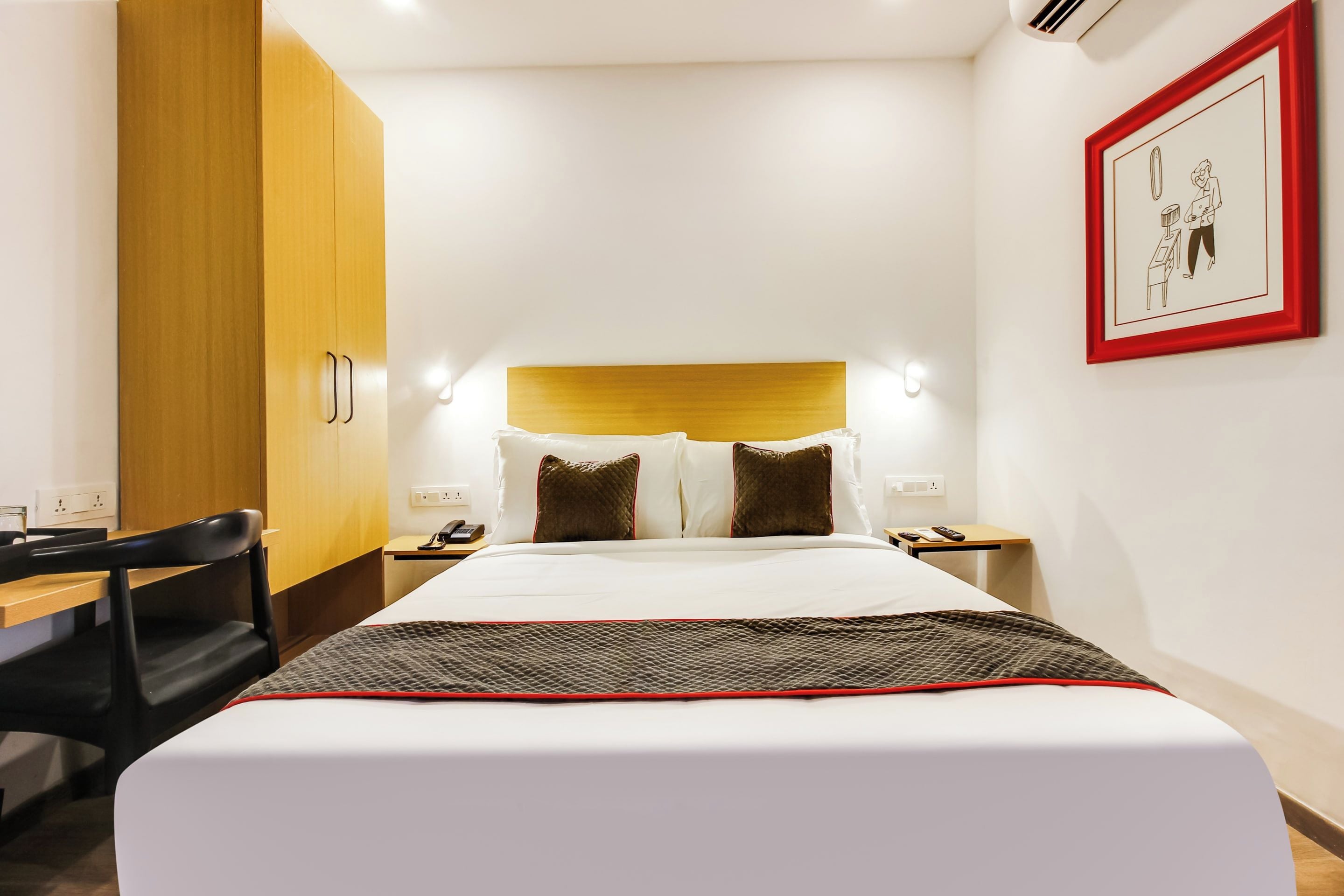 A hotel room with a bed, bedside tables, a desk, and a wardrobe.