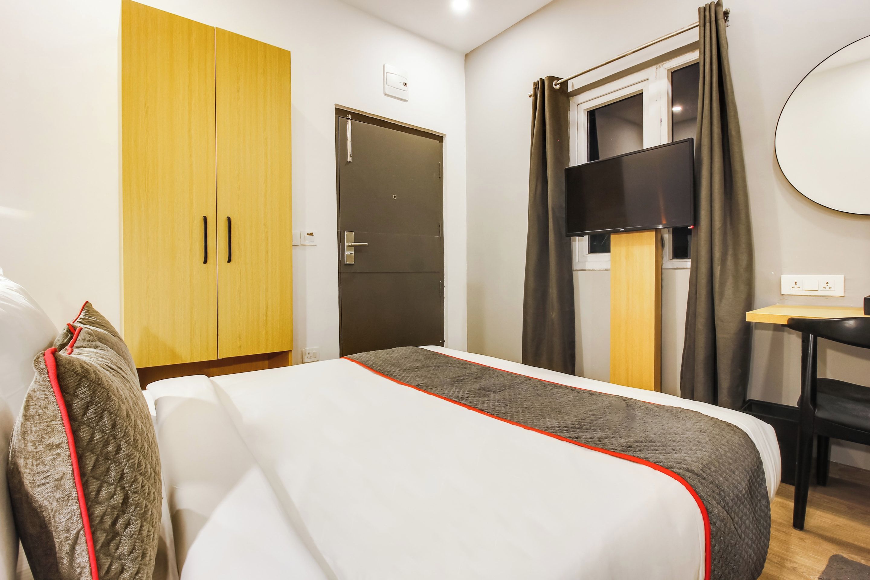 Quarto de hotel com cama, escrivaninha, televisão e armário.