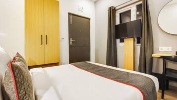 Quarto de hotel com cama, escrivaninha, televisão e armário.