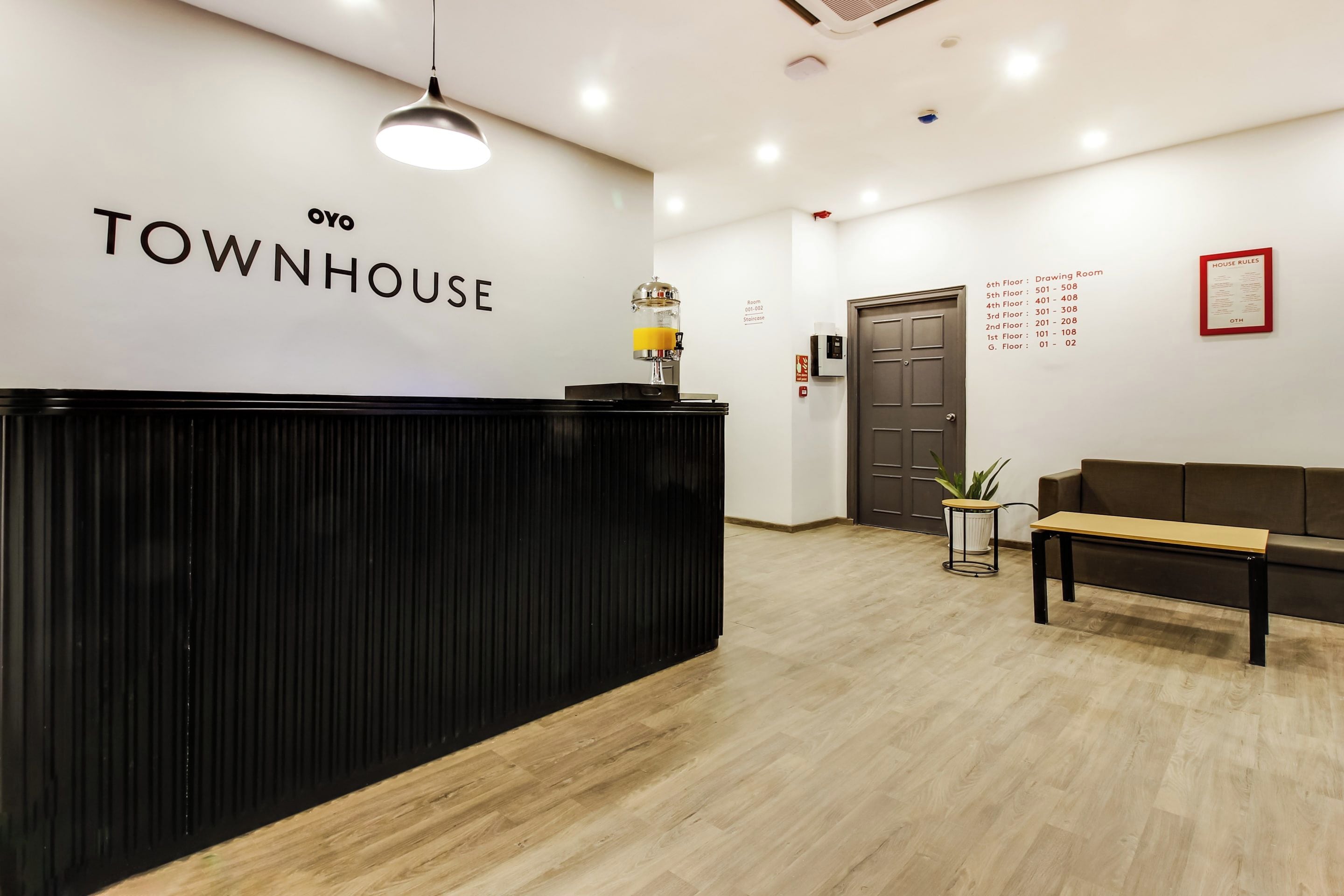 A reception desk with a sign reading 'TOWNHOUSE' and a wall-mounted 'HOUSE RULES' sign listing room numbers and floor assignments.
