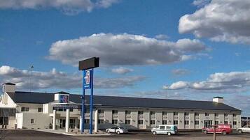 Ein Motel mit großem Parkplatz, einem blauen Schild und einem Gebäude mit flachem Dach.