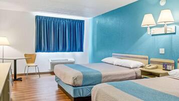 Ein Hotelzimmer mit zwei Betten, einem Schreibtisch, einem Sessel, einem Fenster mit Vorhängen und Wandlampen.