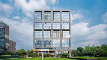 Un edificio moderno de varios pisos con fachada de vidrio, rodeado por un césped cuidado y árboles.