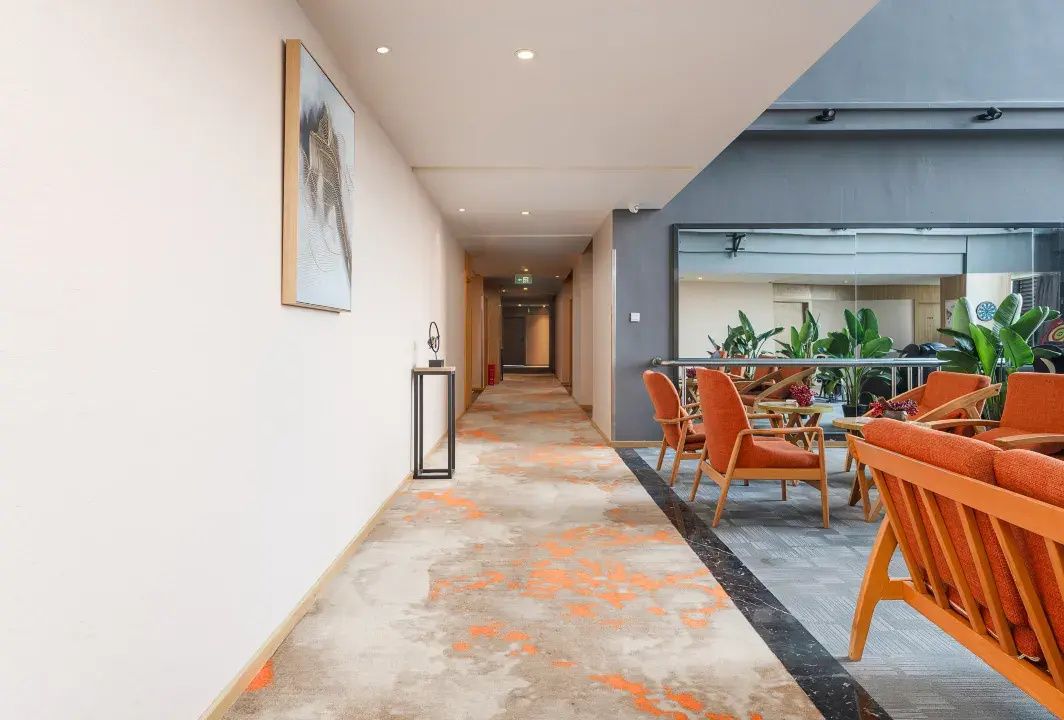 A hotel corridor with a dining area featuring orange chairs and a modern design.