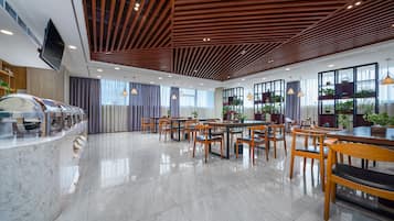 Un comedor amplio con mesas y sillas de madera, una encimera de mármol y ventanas grandes con cortinas.