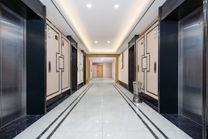 Un pasillo de hotel con ascensores, un cubo de basura y una puerta al final.