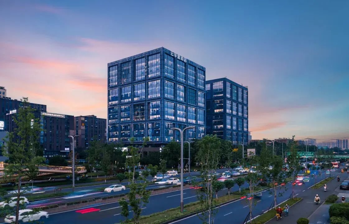 A modern building with multiple floors and a glass facade, surrounded by a busy urban street with vehicles and pedestrians.