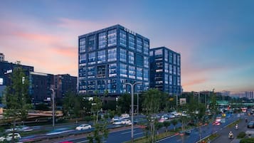 A modern building with multiple floors and a glass facade, surrounded by a busy urban street with vehicles and pedestrians.