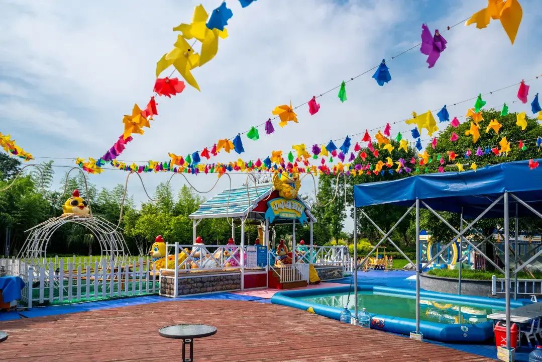 Zona de parque de atracciones al aire libre con piscina, estructuras inflables y un área de juegos cercada.