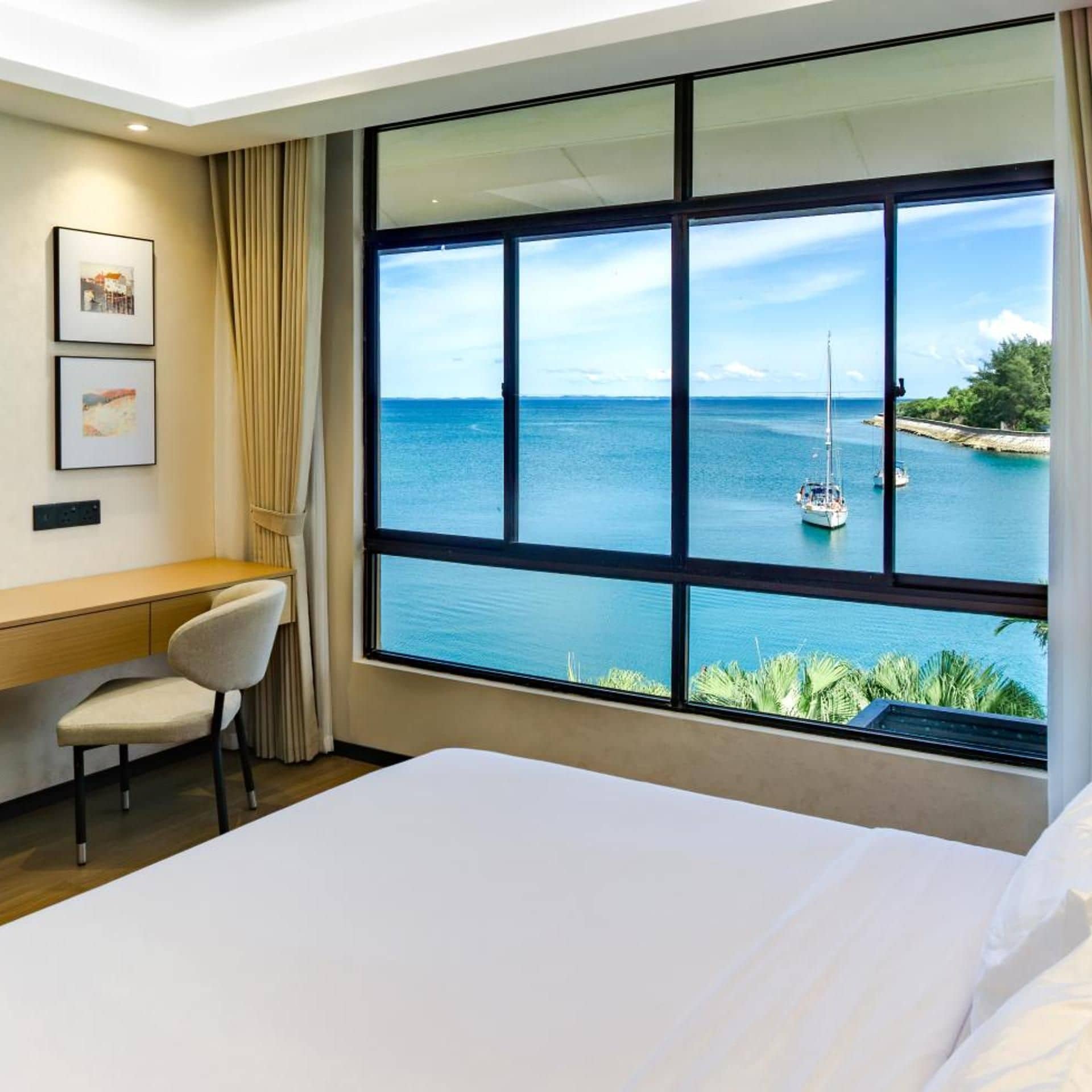 A hotel room with a large window offering a view of the sea and a sailboat.