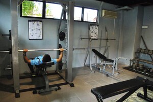 Uma academia com aparelho de supino, suporte para agachamento e diversos pesos.