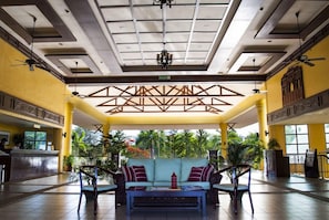 A lobby with a reception desk, a sofa with cushions, and a ceiling fan.
