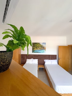 Een hotelkamer met twee bedden, een grote potplant, een schilderij van een landschap en een houten garderobe.