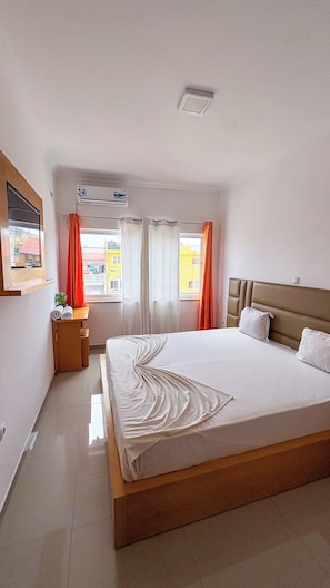 Een hotelkamer met een groot bed, een nachtkastje, een raam met gordijnen en uitzicht op gebouwen.