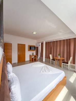 Een hotelkamer met een groot bed, een bureau, een stoel, een televisie en een airconditioning.