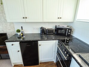 A kitchen with white cabinets, a black countertop, a dishwasher, a toaster, a kettle, and a stove. - Cherry Park Retreat (Skegness)