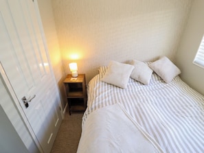 A bedroom with a bed, pillows, a nightstand with a lamp, and a door. - Cherry Park Retreat (Skegness)