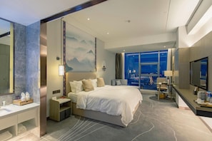 A modern hotel room with a large bed, a desk, a TV, and a view of the cityscape at night. - Argyle Hotel (Honghe)