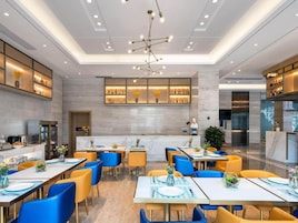 Un restaurante moderno con varias mesas y sillas, una lámpara central y una zona de bar con estanterías.