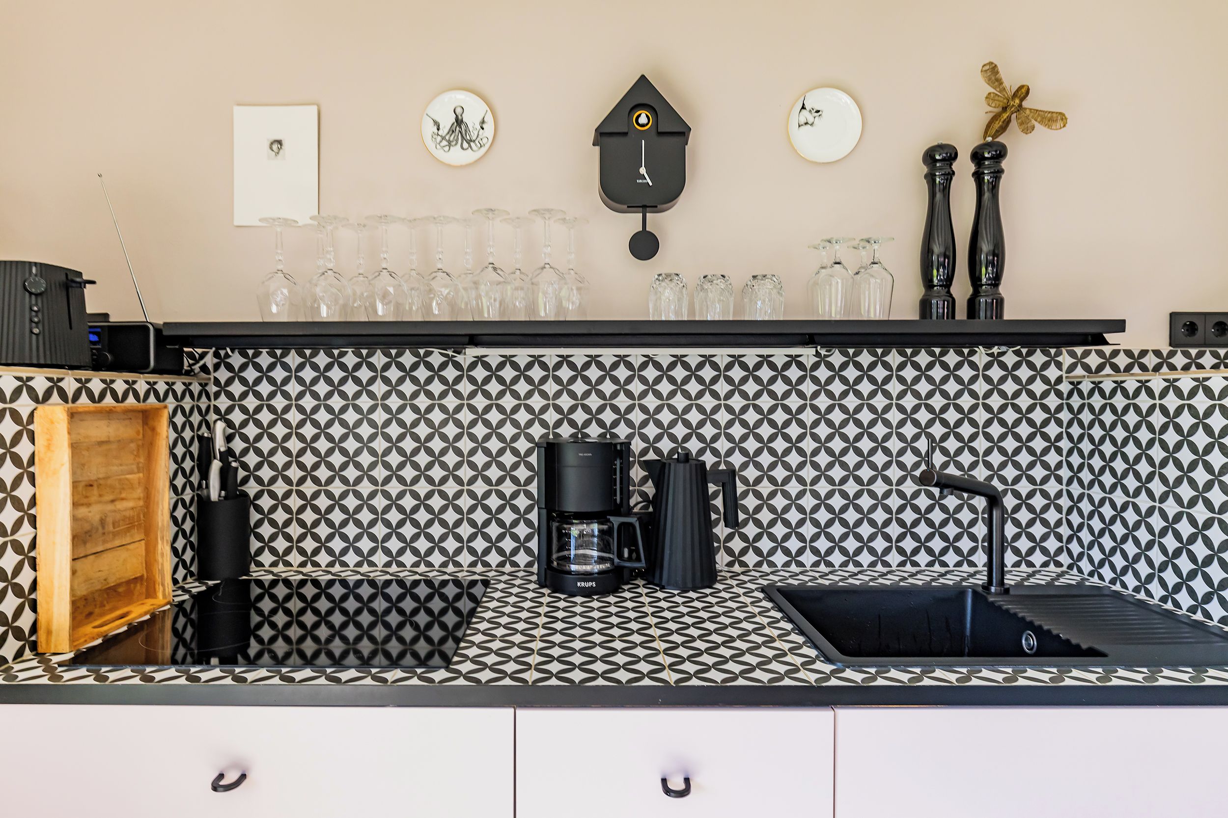 Eine Küche mit einem schwarz-weißen Spritzschutz, einer Kaffeemaschine, einem Spülbecken und einer an der Wand montierten Uhr.
